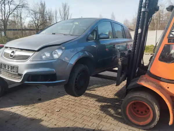 Szary Opel Zafira na złomowisku, podnoszony przez wózek widłowy. Dowiedz się, ile kosztuje złomowanie auta.