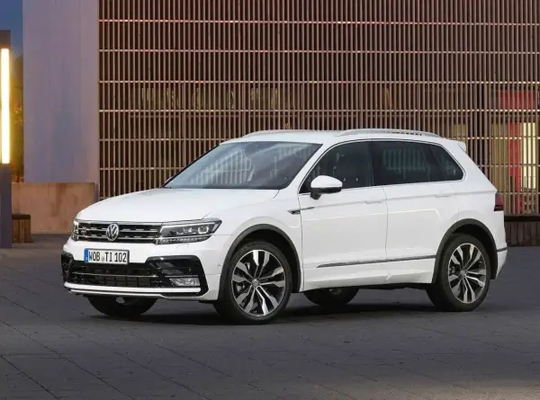 Biały Volkswagen Tiguan 2019 z eleganckimi felgami stoi przed nowoczesnym budynkiem z drewnianą fasadą.