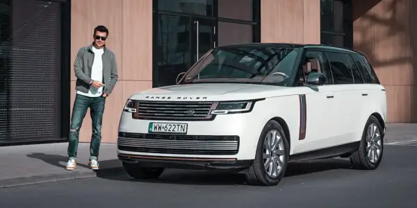 Elegancki mężczyzna obok białego Range Rovera. Sprawdź aktualną range rover cena i dowiedz się więcej o tym luksusowym SUV-ie.