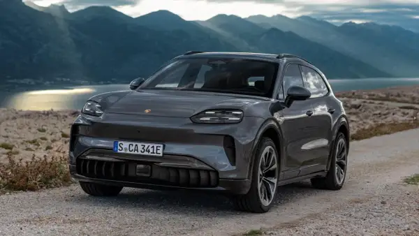 Szary Porsche Cayenne 2025 na kamienistej drodze z widokiem na góry i jezioro.