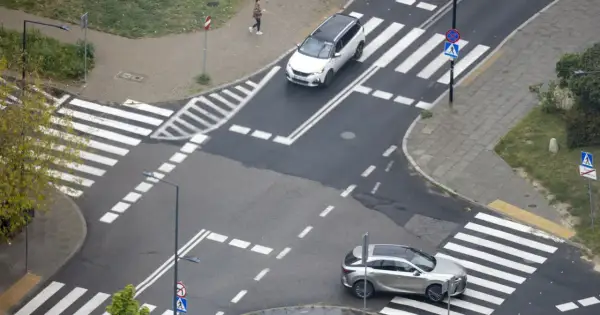 Skrzyżowanie z pasami i znakami drogowymi. Samochody zbliżają się do przejść, stosując zasadę prawej ręki.