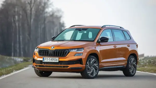 Pomarańczowy Skoda Karoq Sportline na drodze, z drzewami w tle.