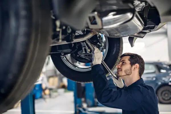 Mechanik w rękawiczkach naprawia podniesiony samochód. Zastanawiasz się, ile zarabia mechanik?