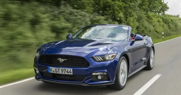 Błękitny mustang cabrio pędzi po krętej drodze wśród zieleni.