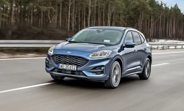 Niebieski Ford Kuga z silnikiem 1.5 Ecoboost pędzi po autostradzie wśród drzew.
