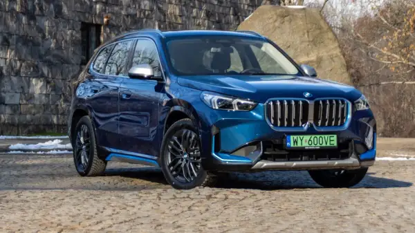 Błękitny BMW X1 elektryk z niebieskimi akcentami na progu, zaparkowany na kamienistej nawierzchni.