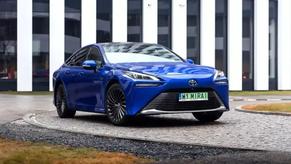 Niebieska Toyota Mirai, samochód przyszłości, zaparkowana przed nowoczesnym budynkiem.